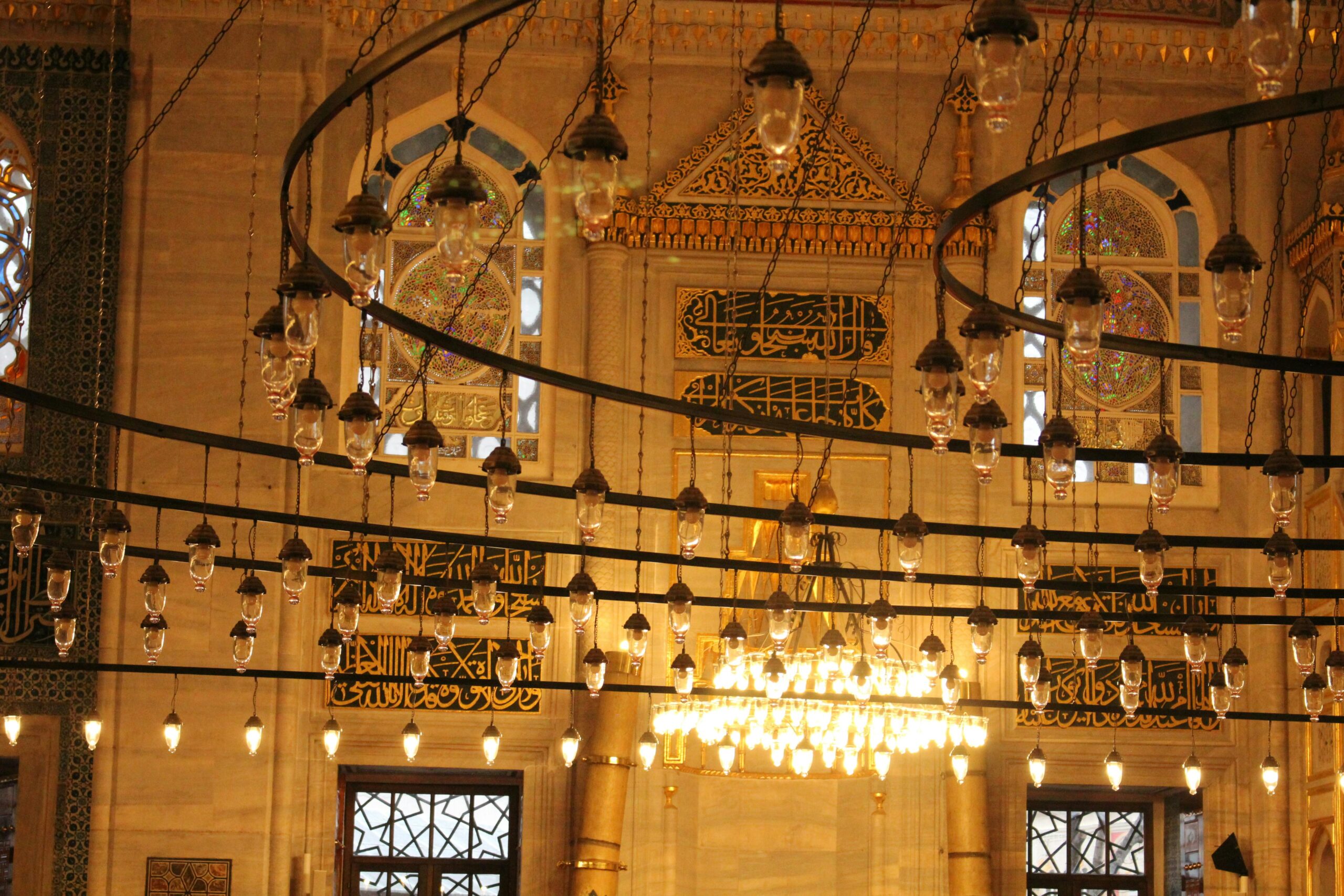 Intricate chandeliers and Arabic calligraphy in a historic mosque interior.